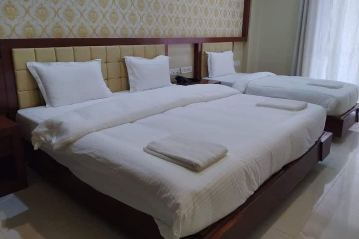 A hotel room with three beds, a wooden headboard, and a patterned wallpaper.