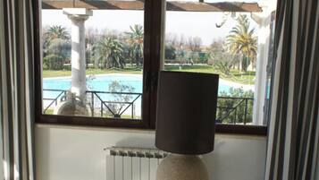 A room with a large window overlooking a pool and greenery. There is a textured vase on a pedestal table.