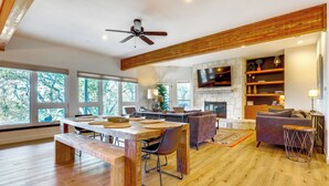 A spacious living area with a wooden dining table, a sofa, and a fireplace. - Modern Fischer House w/ Deck, Fire Pit & Hot Tub! (Fischer)
