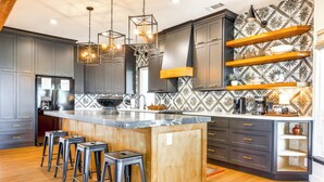 A modern kitchen with a central island, bar stools, and a patterned backsplash. - Modern Fischer House w/ Deck, Fire Pit & Hot Tub! (Fischer)