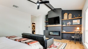 A modern bedroom with a bed, a sofa, a TV, a fireplace, and a desk area. - Modern Fischer House w/ Deck, Fire Pit & Hot Tub! (Fischer)