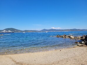 A coastal scene with a cruise ship, rocky shoreline, and distant hills.
