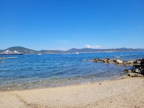A beach with clear water, a rocky shoreline, and distant mountains.