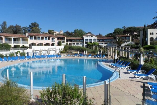 A swimming pool surrounded by lounge chairs and a building with multiple balconies.