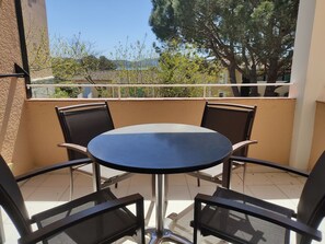 A round table with four chairs on a balcony with a view of trees and a building in the background.
