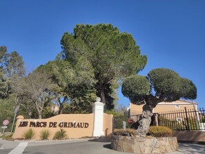 A sign for 'Les Parcs de Grimaud' with a large tree and a stone planter in the foreground.