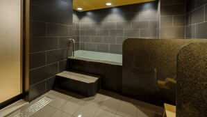 A modern bathroom with dark tiles, a granite countertop, and a step leading to a bathtub. - Tosei Hotel Cocone Asakusa Kuramae (Tokyo)