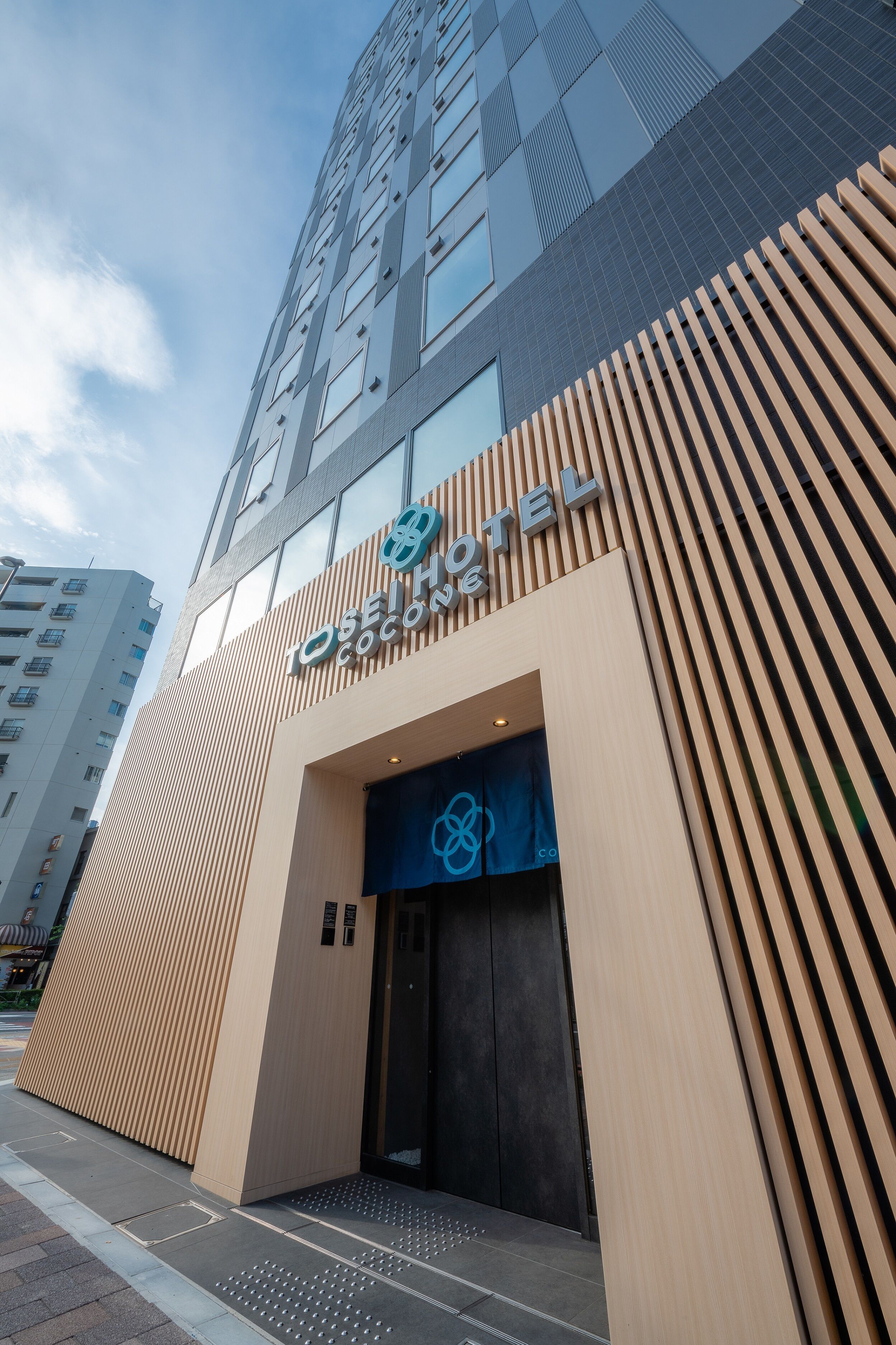 A modern hotel entrance with a prominent sign, a large glass facade, and a wooden slatted design on the side.