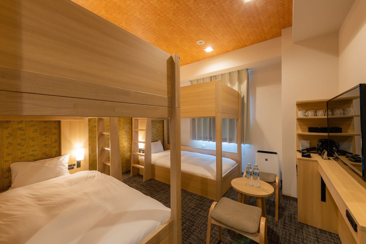 A hotel room with two beds, a desk, a chair, a small table with water bottles, and a television.