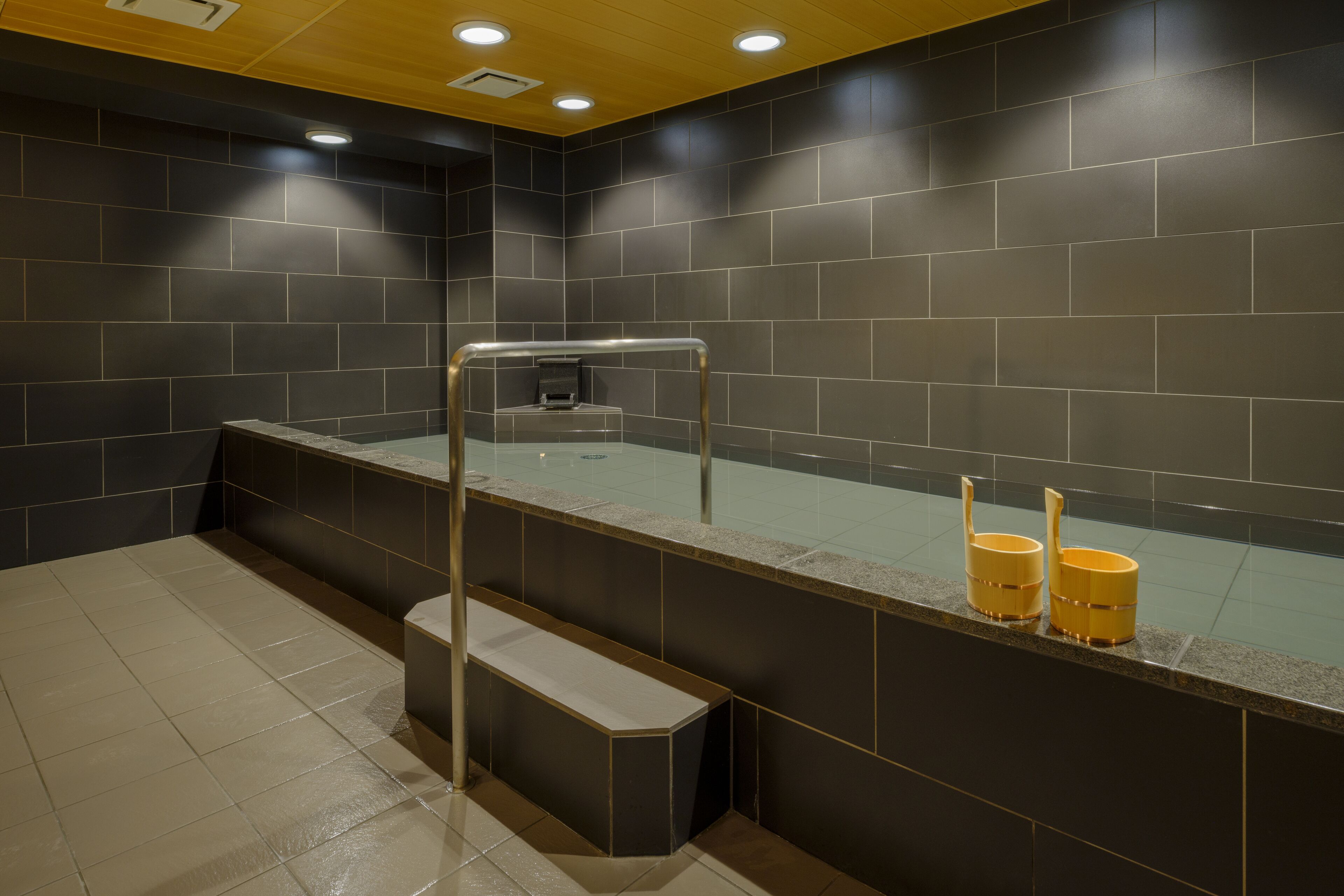 A modern bathroom with dark tiled walls, a glass shower enclosure, and a bench.