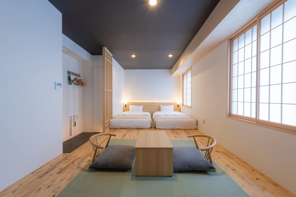 A room with two beds, a wooden table, and a view through a large window.