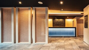 A reception area with a wooden reception desk, a wall-mounted sign, and a patterned partition. - Tosei Hotel Cocone Asakusa Kuramae (Tokyo)
