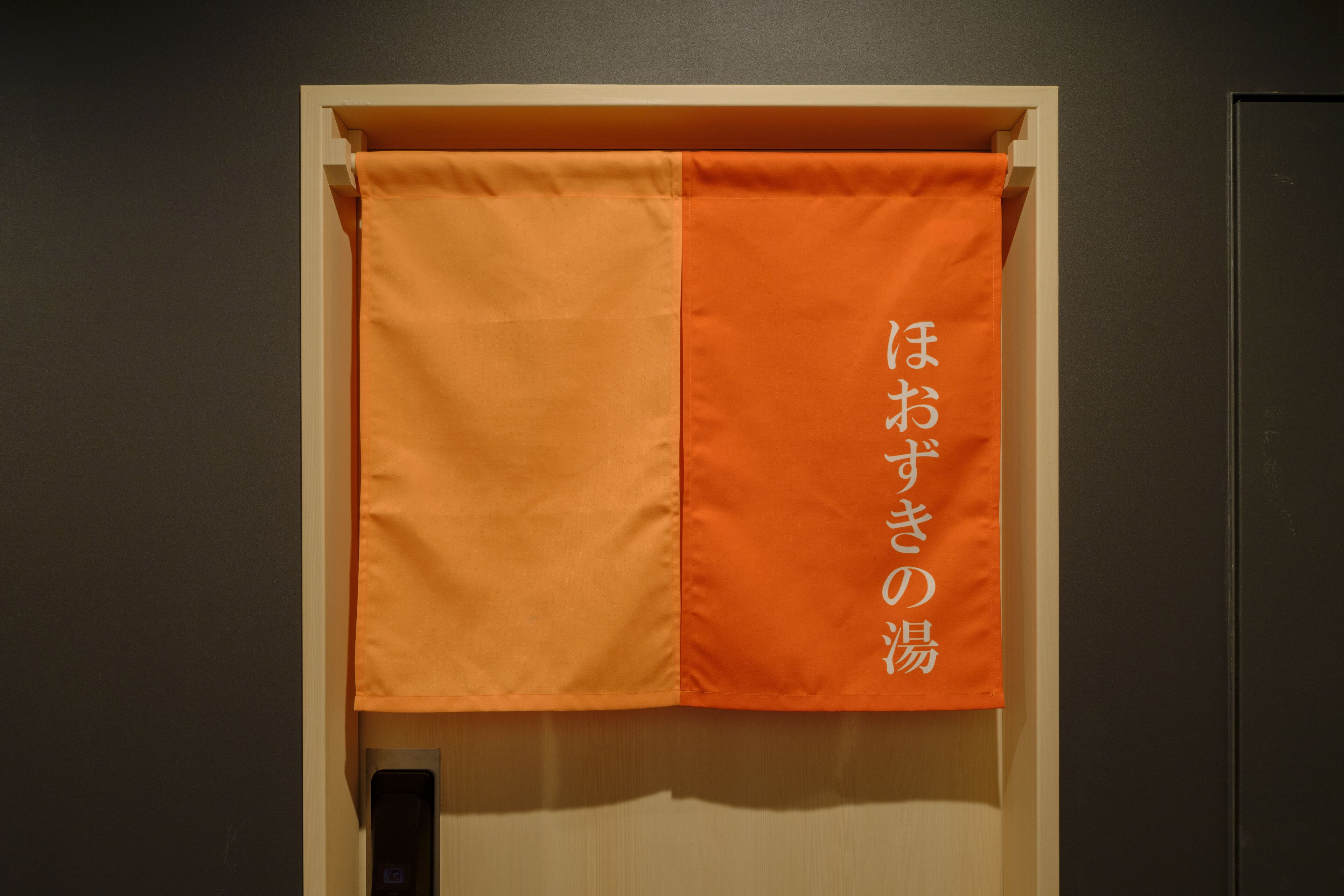 Una habitación con una puerta y una cortina anaranjada y blanca con texto en japonés.