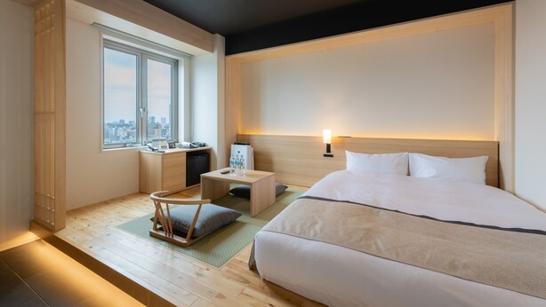 A hotel room with a large bed, a desk with a chair, a small table, a nightstand, and a window with a city view. - Tosei Hotel Cocone Asakusa Kuramae (Tokyo)
