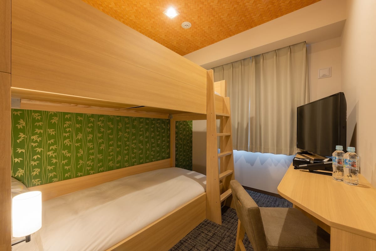 A bunk bed room with a desk, TV, and two bottles of water.