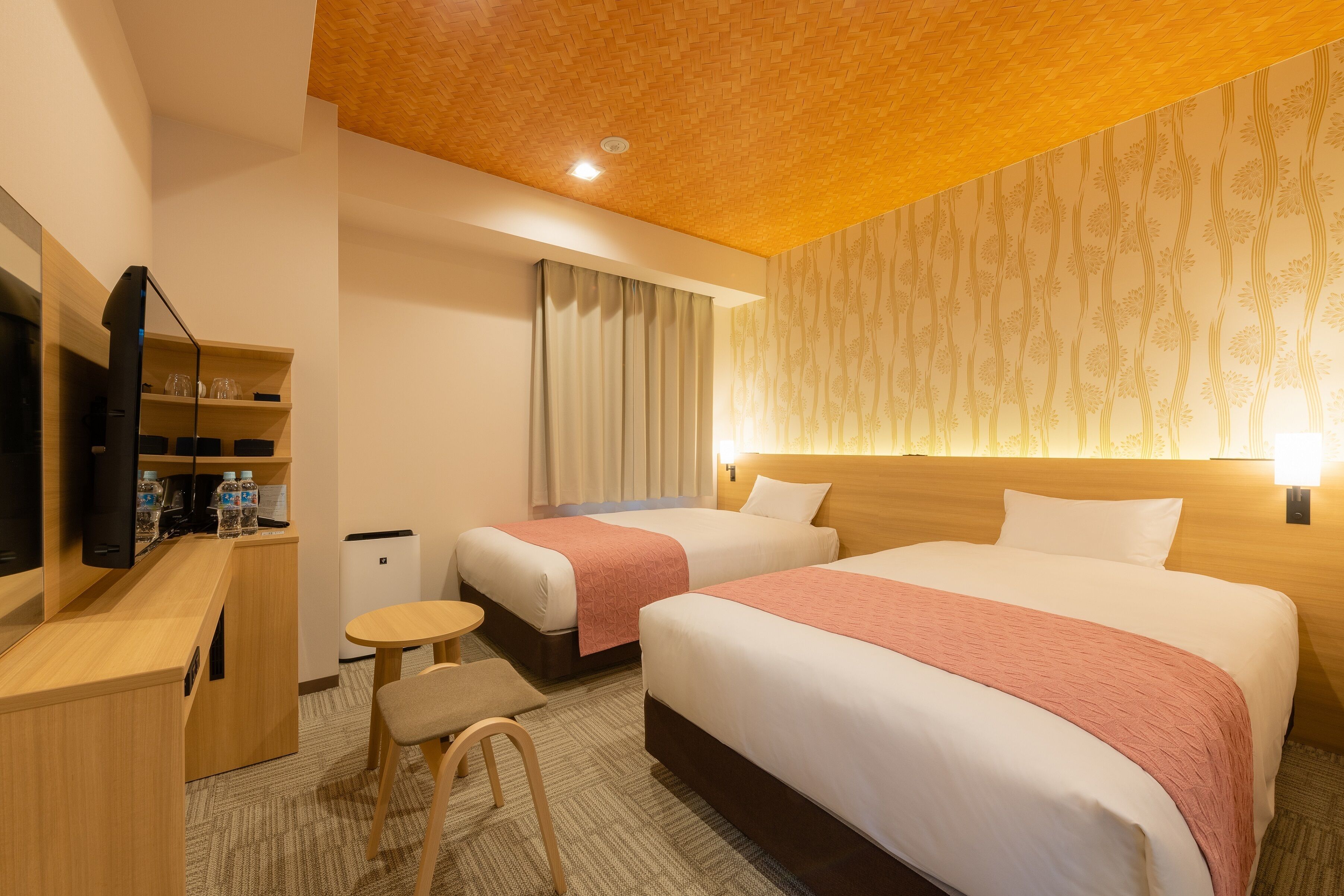 A hotel room with two beds, a desk, a TV, and a small table.