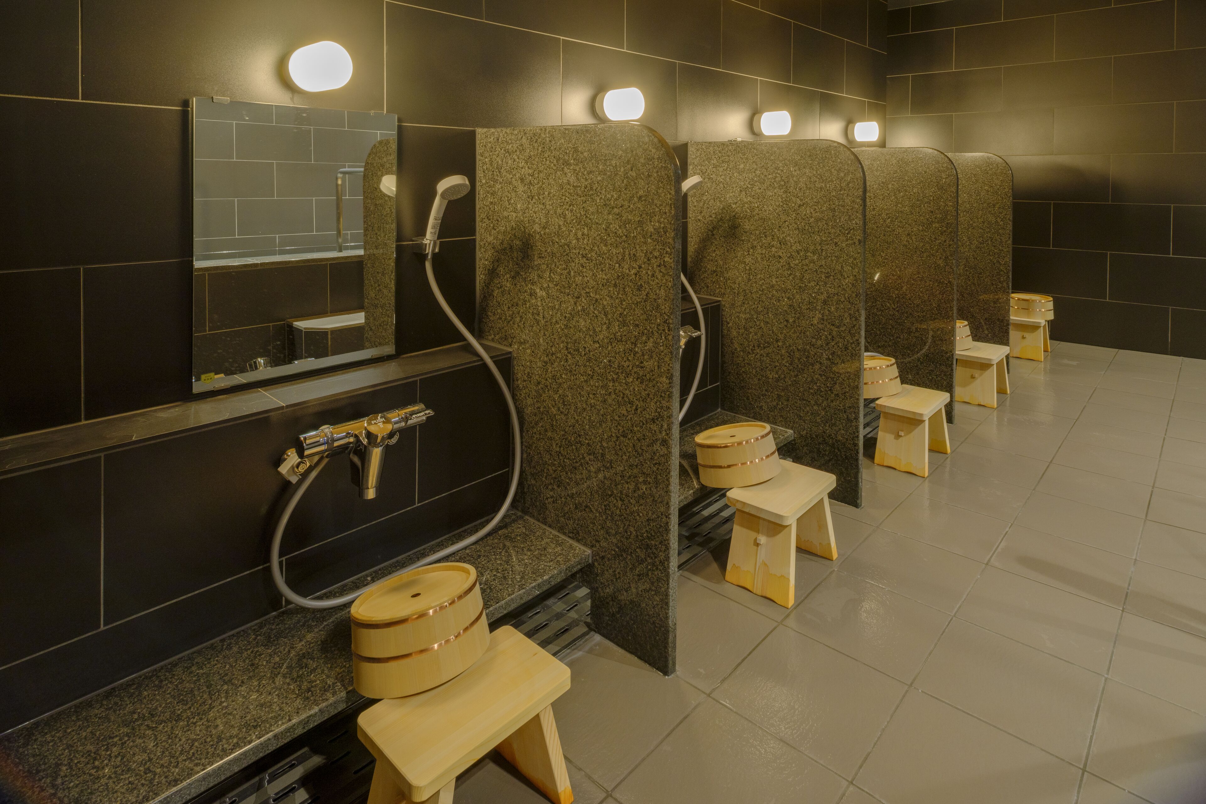 Een openbaar toilet met meerdere cabines, elk voorzien van een toilet, een wastafel en een spiegel.