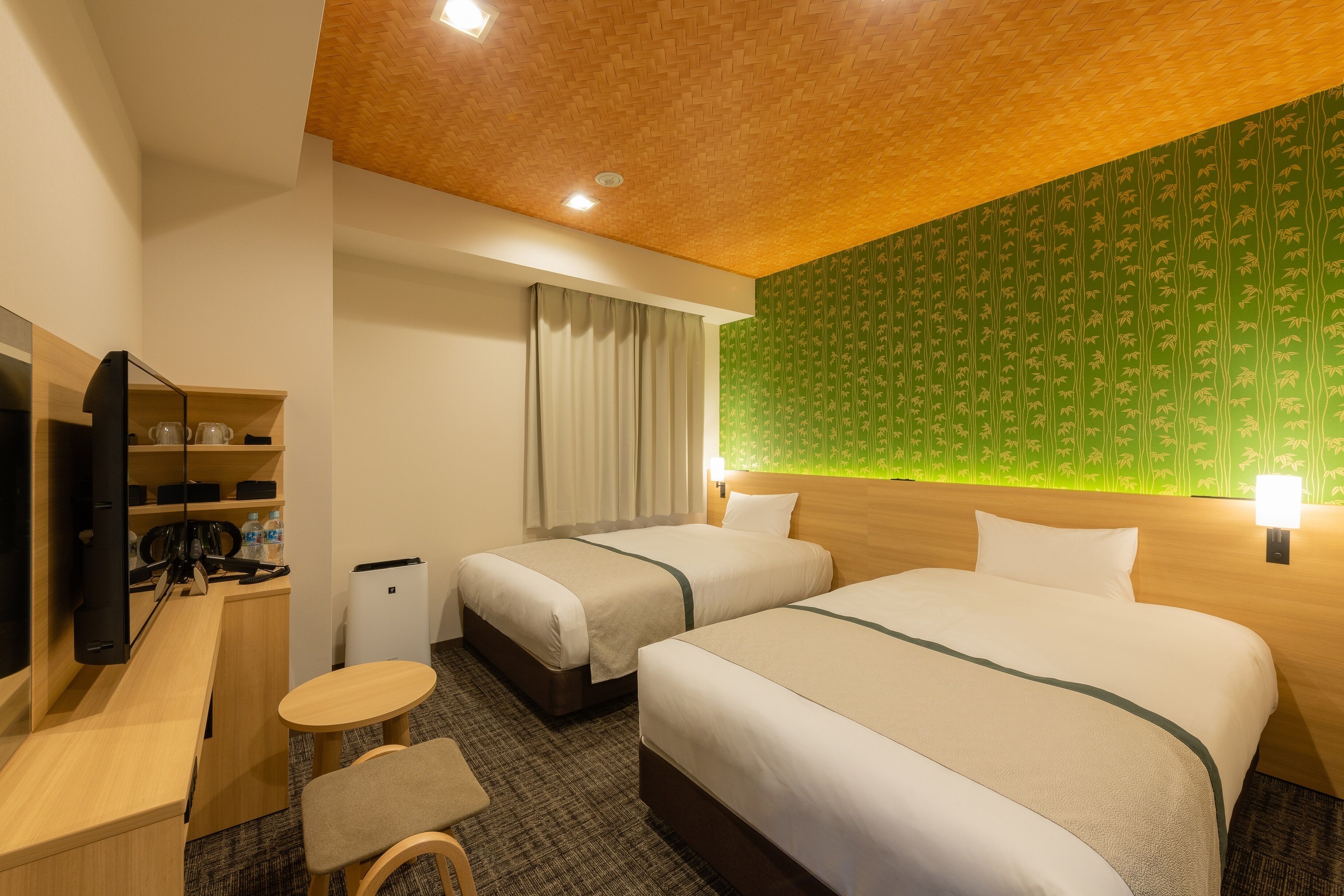 A hotel room with two beds, a desk, a chair, a small table, and a television.