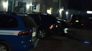 A nighttime parking area with several cars parked in front of a building with multiple windows and air conditioning units.