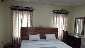 A hotel room with a large bed, two white pillows, a wooden headboard, and a desk with a chair.