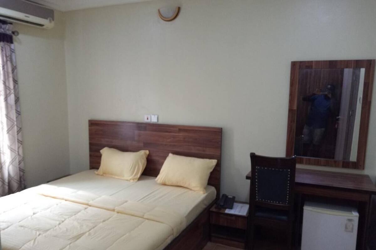 A bedroom with a bed, a desk, a chair, and a small refrigerator.