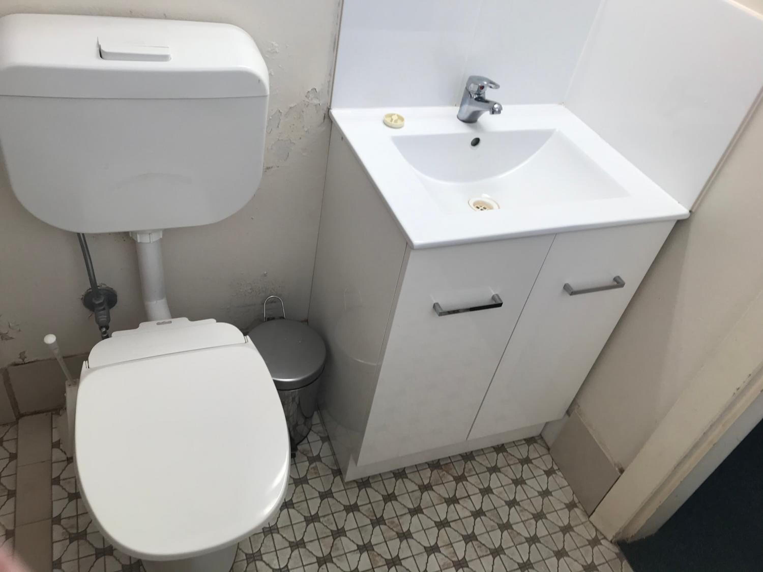 A small bathroom with a toilet, a sink, and a cabinet.