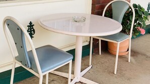 Ett runt, vitt bord med en enkel askkopp i glas, omgivet av två stolar i vintage-stil med vadderade sitsar och metallramar.