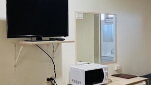 Ett rum med en platt-TV som är monterad på väggen, en mikrovågsugn på en liten bänk och ett kylskåp.