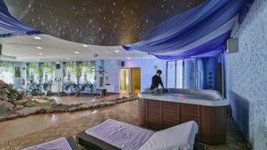 Ett spaområde med ett bubbelbad, massagebänkar, träningsutrustning och ett dekorativt tak.