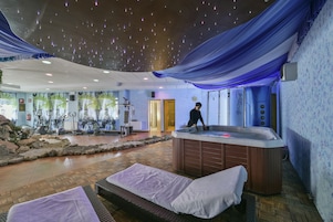 Zona de spa con hidromasaje, mesas de masaje, equipo de ejercicio y techo decorativo.