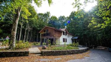 Uma casa de dois andares com alicerce de pedra, rodeada por uma floresta.