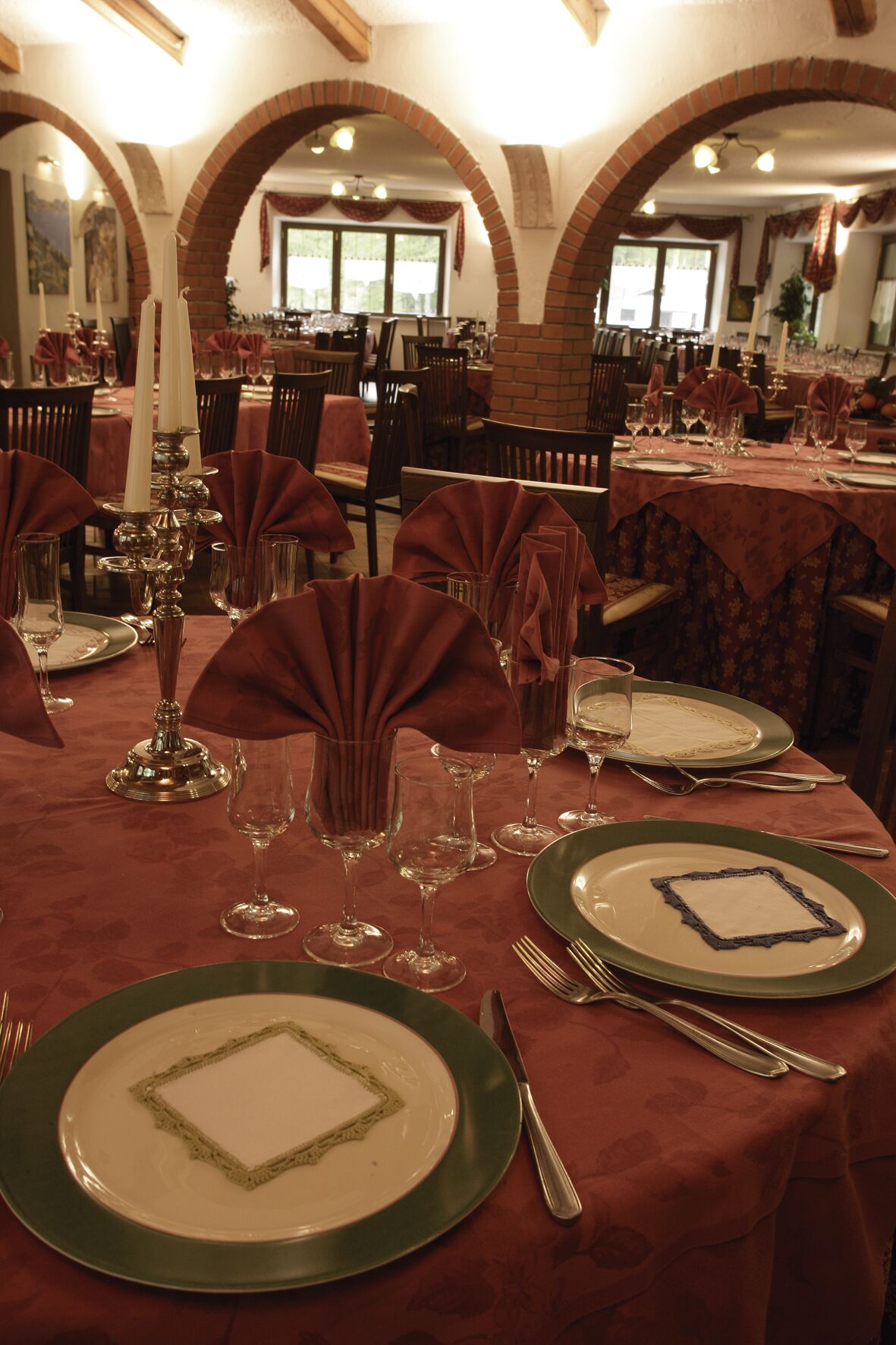 A restaurant with tables set for dining, featuring green plates and red tablecloths.