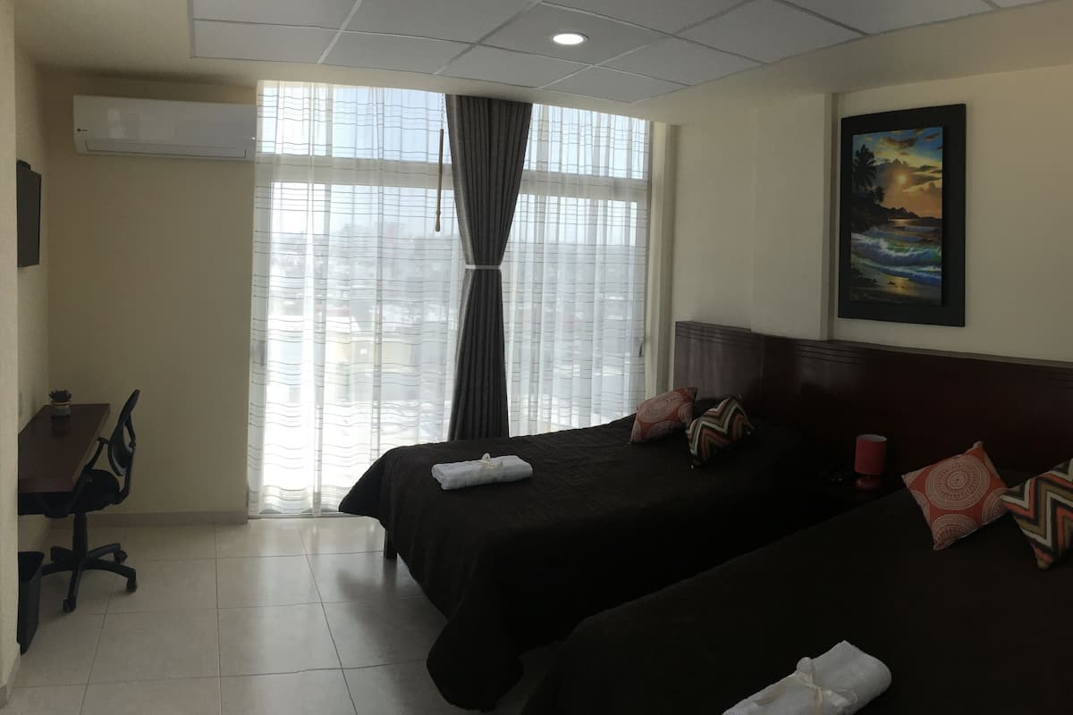 A hotel room with two beds, a desk, and a window with curtains.