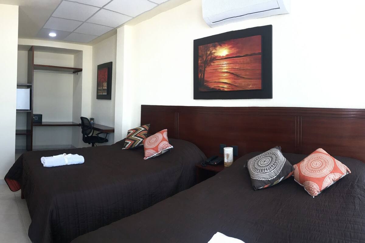 A hotel room with two beds, a TV, a painting, and a desk with a chair.