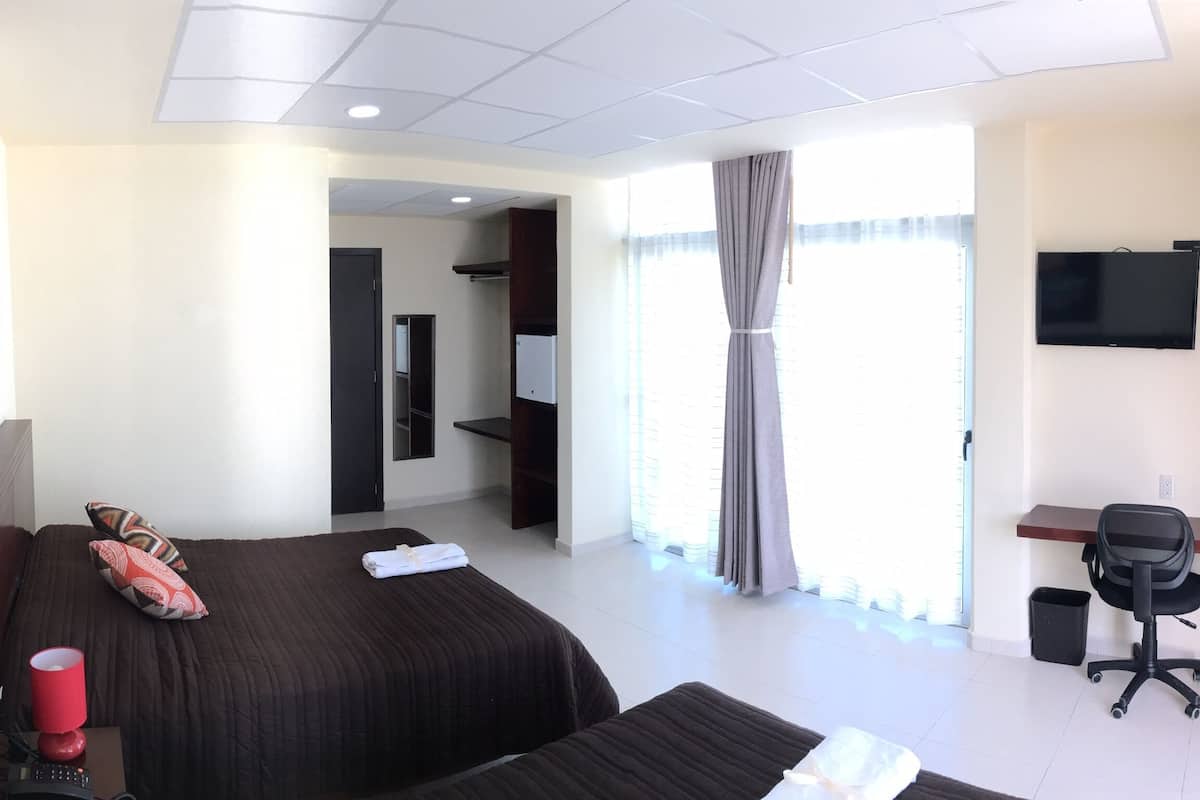 A hotel room with two beds, a desk with a chair, a TV, and a window with curtains.