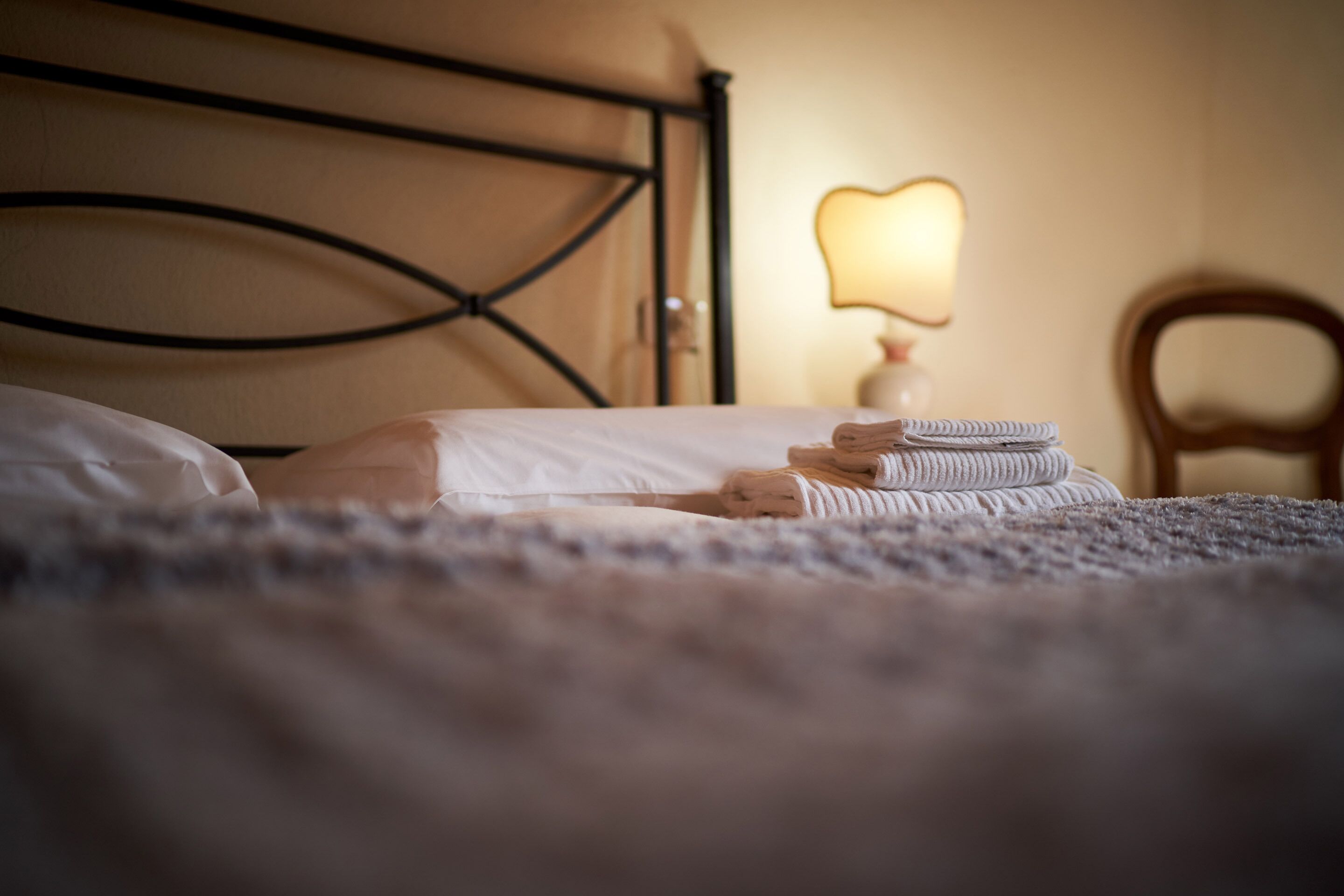 Una cama con cabecera, lámpara de noche y una silla.