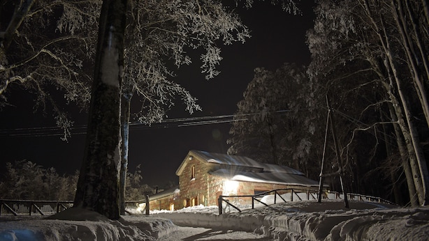 A snow-covered landscape with a wooden cabin and a fence.