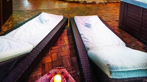 Two massage beds with towels, a hot tub, and a stone garden in the background.