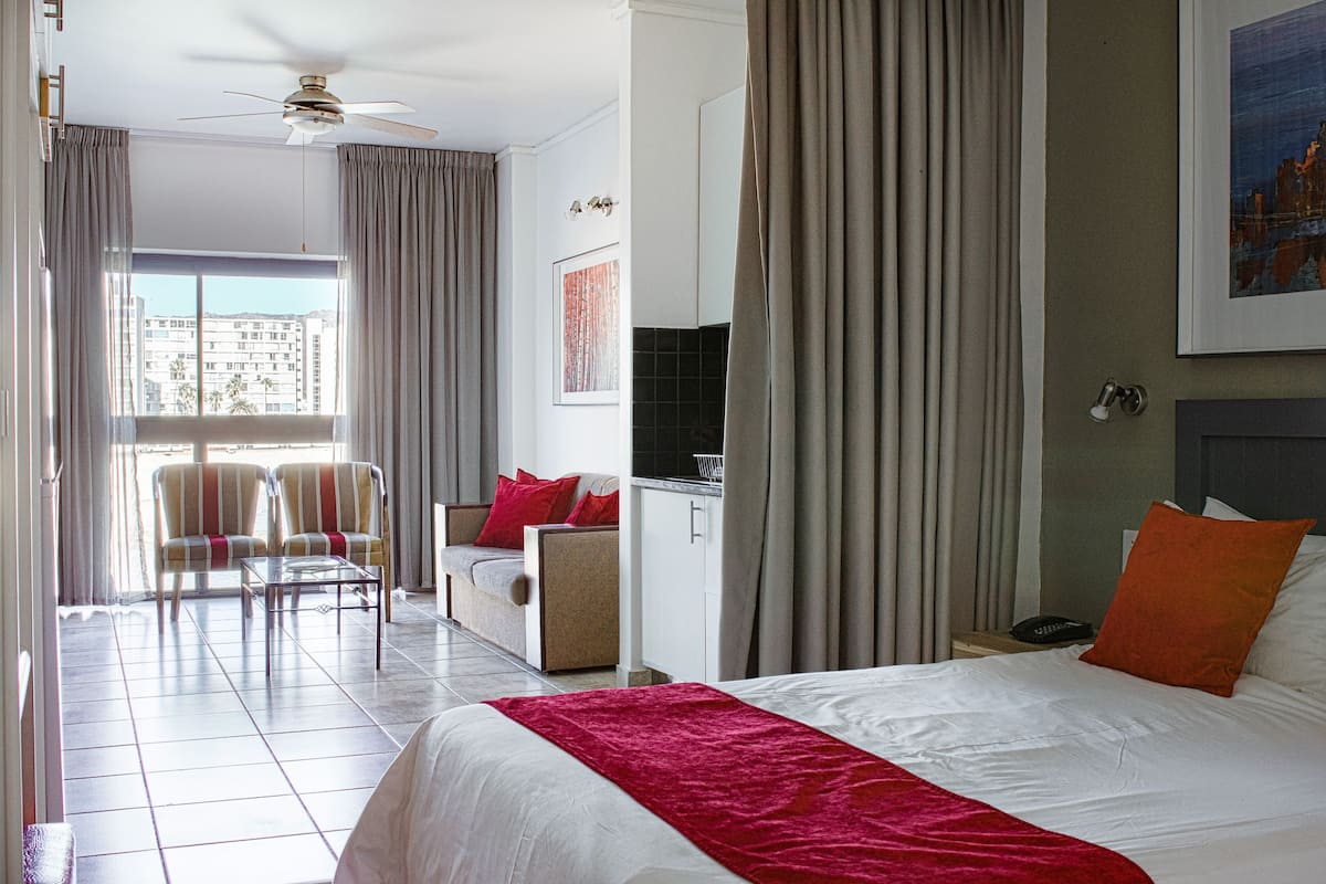 A hotel room with a bed, a desk, a chair, a sofa, and a view of the city through the window.
