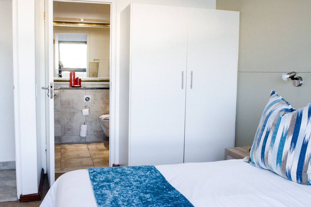 A hotel room with a bed, a wardrobe, a nightstand, a bathroom with a toilet and sink, and a mirror.