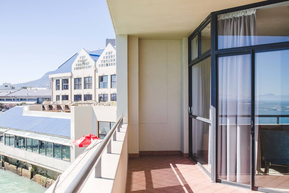 A balcony with a view of a building with a sloped roof and a mountain in the background.