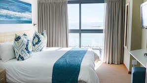 A hotel room with a large bed, a view of the sea, and a TV on the wall.