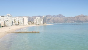 A beachside hotel with multiple buildings, a sandy beach, and mountains in the background.