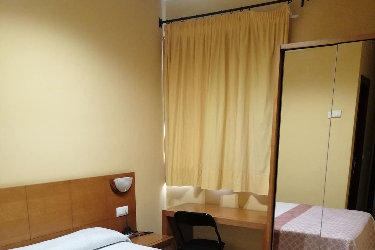 A hotel room with two beds, a desk, a chair, and a mirror.