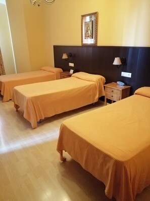 A hotel room with three single beds, wooden nightstands, a wall-mounted lamp, and a framed picture above the headboard. - Hostal La Isla (Montijo)