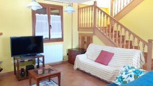 Una sala de estar con televisor, sofá, mesa de centro y escalera.