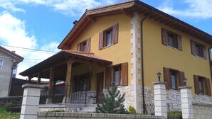 Un edificio amarillo con porche, pilares de piedra y contraventanas de madera.