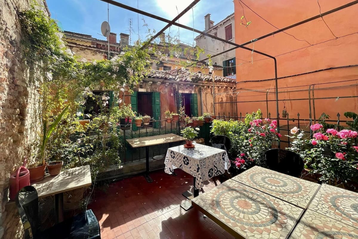 A courtyard with a tiled table, potted plants, and a view of buildings in the background.