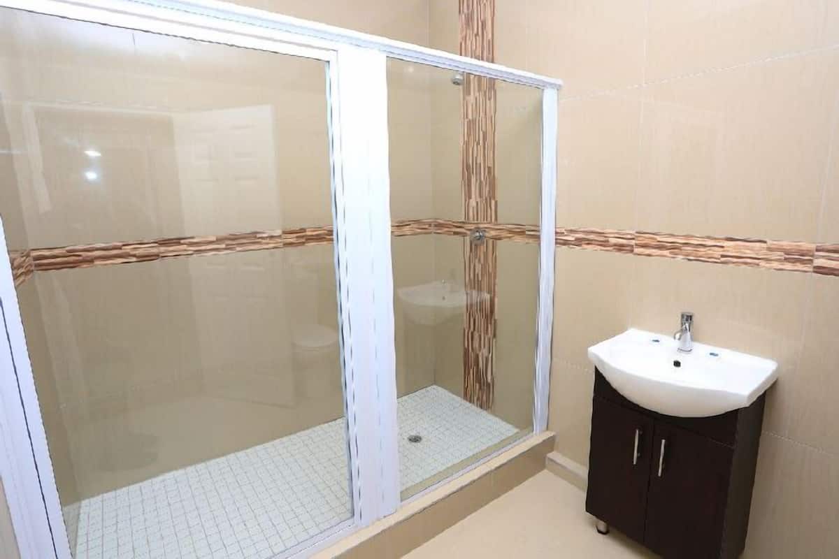 Een badkamer met een glazen douchecabine, een wastafel en een kast.