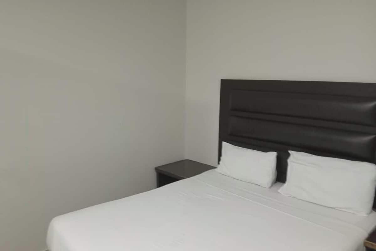 Een enkel bed met een donker hoofdbord, wit beddengoed en een klein nachtkastje.